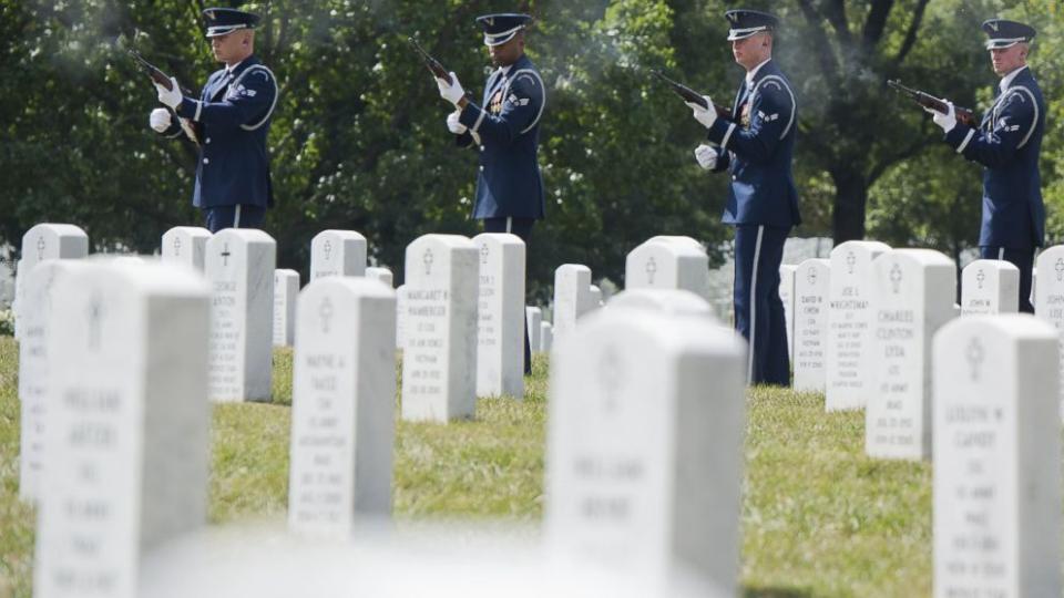 A group of military men are standing in a cemetery, paying tribute to their fallen comrades.