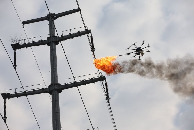 Update: A drone is flying over a power line with flames coming out of it.