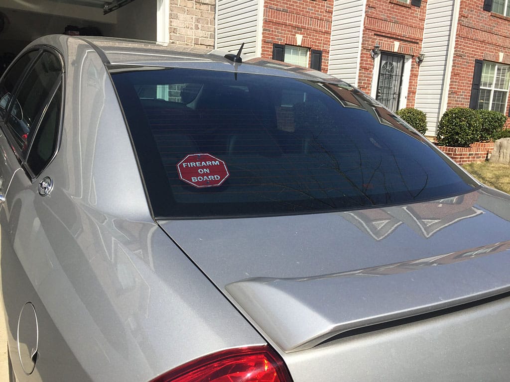 A silver car with a stop sign sticker on the back, undergoing recall.