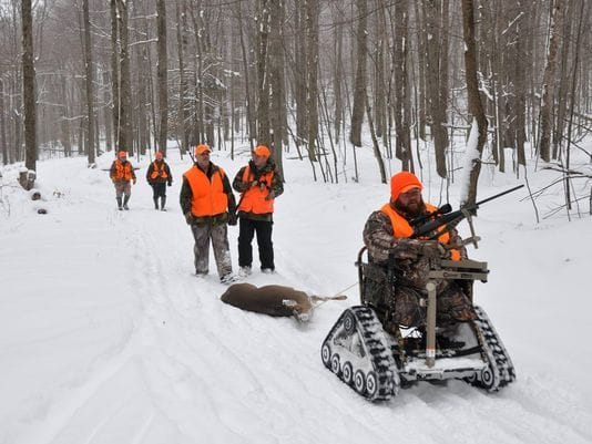 A group of hunters on a snowmobile training in the woods.