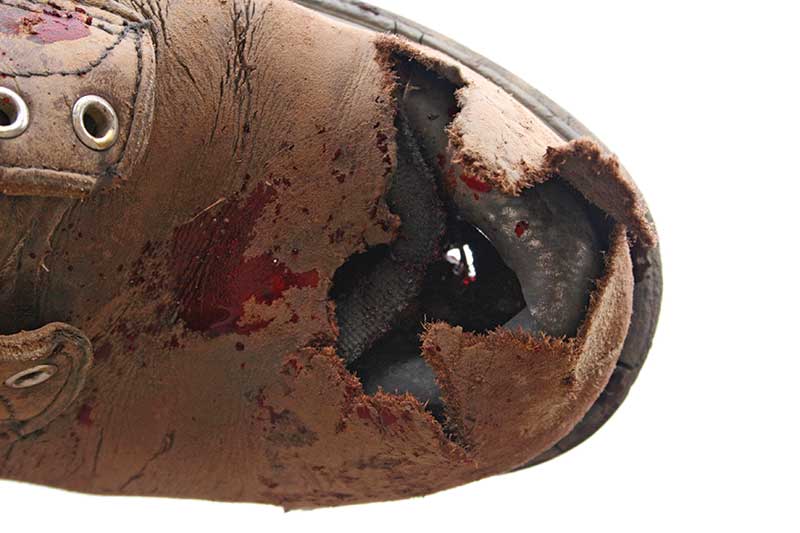 Close-up of a worn-out brown shoe with a torn toe and visible inner lining.
