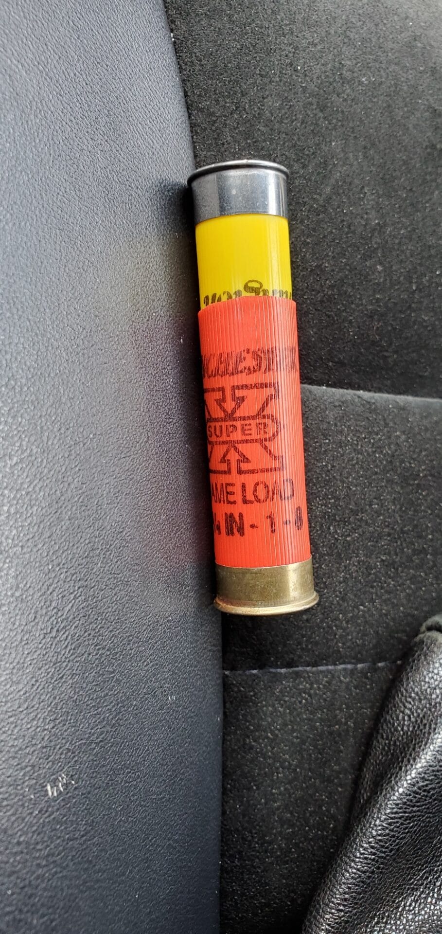 A yellow and red shotgun shell labeled "12 GA SUPER X GAME LOAD" lies on a black fabric surface.