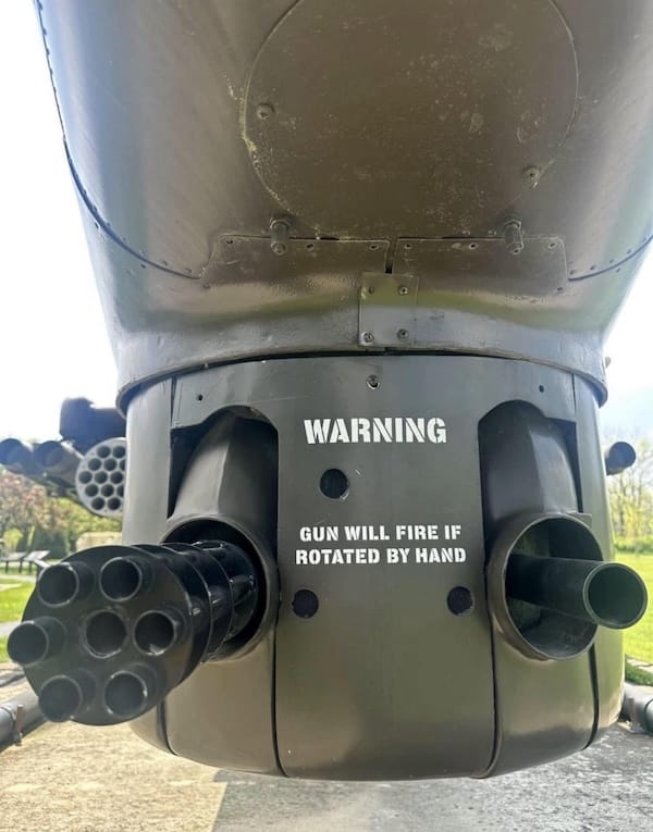 Close-up of a military helicopter's gun with warning text: "Gun will fire if rotated by hand.