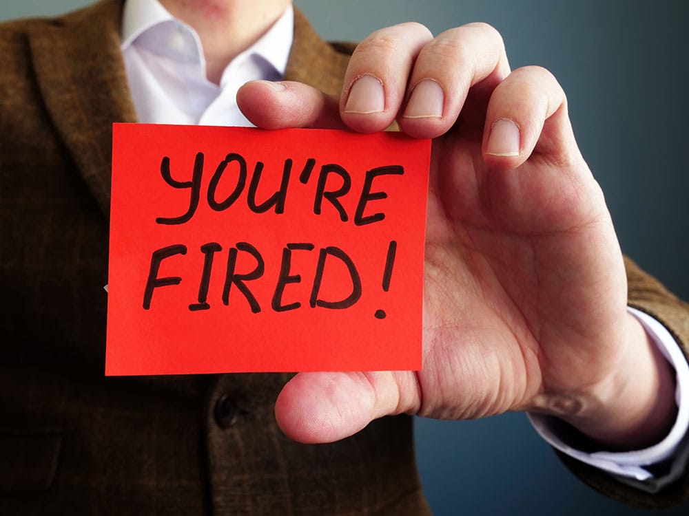 Person holding a red card with the handwritten message "YOU'RE FIRED!" in black letters.